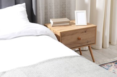 Yatağın yanında kitap ve çerçeve olan komodin.