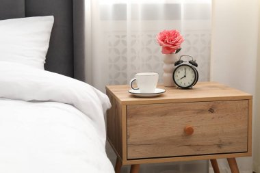 Yatağın yanında kahve, çiçek ve çalar saat olan komodinin yanında.