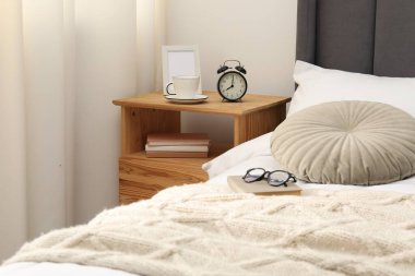 Yatağın yanında çalar saati, kahvesi ve çerçevesi olan bir komodin.