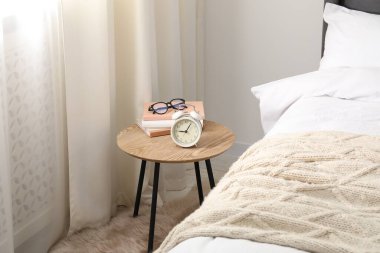 Yatağın yanında çalar saati, kitapları ve bardakları olan bir komodin.