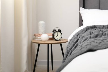 Yatağın yanında alarm saati ve dekorasyonu olan komodinin yanında.