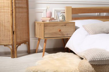 Yatağın yanında çalar saati, kitapları ve dekorasyonu olan bir komodin.