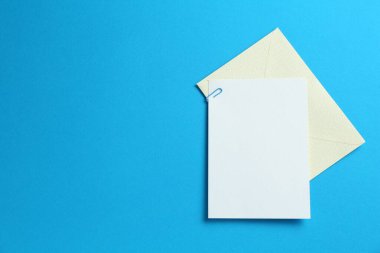 Açık mavi arka planda boş davetiye ve zarf, üst manzara. Tasarım için boşluk