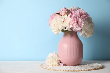 Açık mavi duvarın yanındaki beyaz masada vazodaki güzel şakayıklar. Metin için boşluk