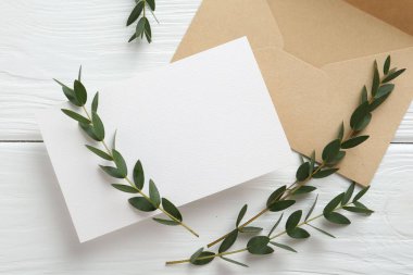 Boş davetiye kartı, zarf ve dallar beyaz ahşap masada, düz yerde. Tasarım için boşluk