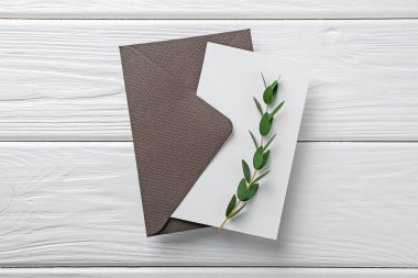 Boş davetiye kartı, zarf ve dal beyaz ahşap masa, üst görünüm
