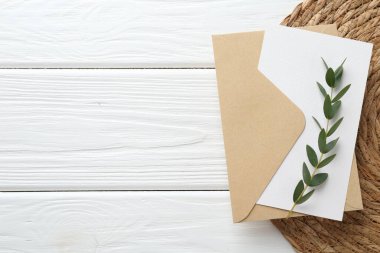 Boş davetiye kartı, zarf, dal ve hasır kaplama beyaz ahşap masa, üst manzara. Metin için boşluk