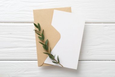 Boş davetiye kartı, zarf ve dal beyaz ahşap masa, üst görünüm
