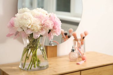 Vazodaki güzel şakayıklar, parfümler, fırçalar ve kapalı alandaki ahşap kibir aynaları.