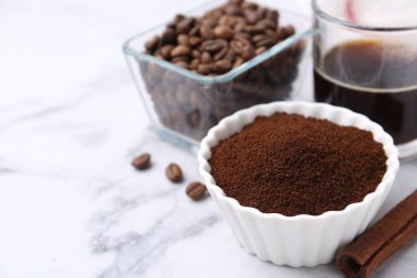 Kasedeki kahve tozu, tarçın çubuğu, fasulye ve içecek beyaz mermer masada, yakın plan. Metin için boşluk