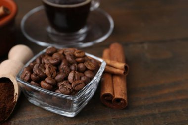 Kavrulmuş fasulye, hazır kahve tozu ve ahşap masada tarçın çubukları, yakın plan.