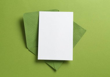 Yeşil arka planda boş davetiye ve zarf, üst manzara. Tasarım için boşluk