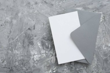 Gri desenli masa üzerinde boş davetiye ve zarf, üst manzara. Tasarım için boşluk