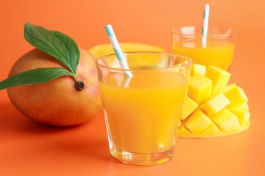 Bardakta lezzetli mango suyu ve turuncu arka planda taze meyve, yakın plan.