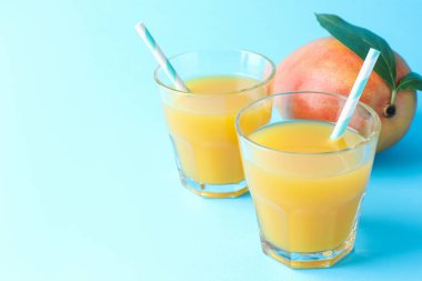 Bardakta lezzetli mango suyu ve açık mavi arka planda taze meyve, yakın plan. Metin için boşluk