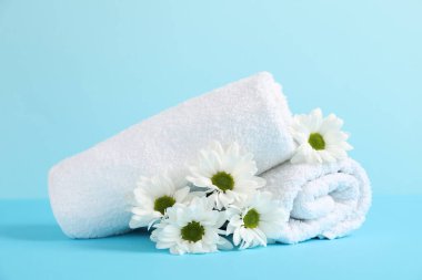 Açık mavi arka planda yumuşak havlular ve kasımpatı çiçekleri