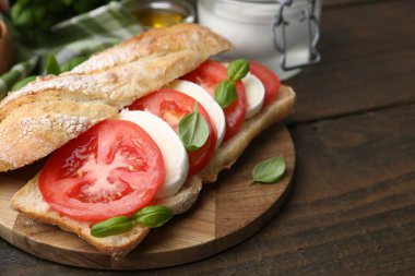 Mozarella peynirli, domatesli ve ahşap masadaki fesleğenli lezzetli sandviç.