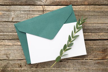 Boş davetiye kartı, zarf ve yeşil dal, ahşap masa, üst manzara.