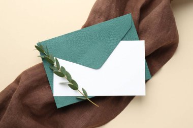 Boş davetiye kartı, zarf ve bej arka planda yeşil dal, üst görünüm