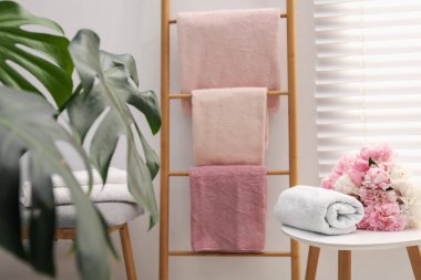 Dekoratif ahşap merdivende yumuşak havlular, şakayık çiçekleri ve banyoda yeşil bitkiler.