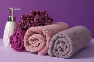 Yumuşak havlular, sıvı sabun ve mor arka planda leylak çiçekleri, yakın plan.