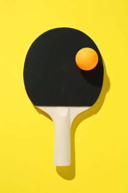 Sarı arka planda pinpon raketi ve top, üst manzara.
