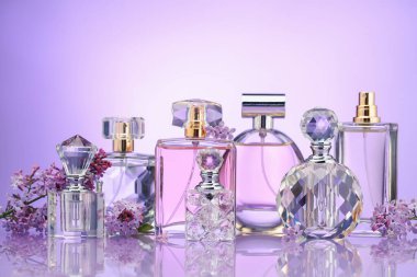 Ayna yüzeyinde mor arkaplana karşı parfüm şişeleri ve leylak çiçekleri