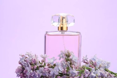 Parfüm şişesi ve mor arka planda leylak çiçekleri, yakın plan.