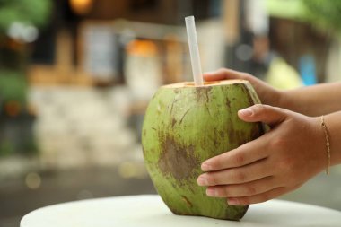 Dışarıdaki masada yeşil hindistan cevizli, ferahlatıcı içecekten içen kadın, yakın plan. Metin için boşluk
