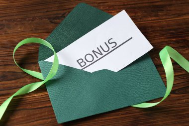 Üzerinde bonus, zarf ve kurdele olan kart ahşap masanın üstünde.