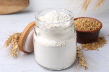 Cam kavanozda buğday unu, beyaz masada tahıl ve çiviler, yakın plan.