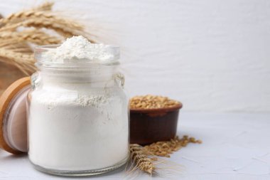Cam kavanozda buğday unu, beyaz masada tahıl ve çiviler, yakın plan. Metin için boşluk
