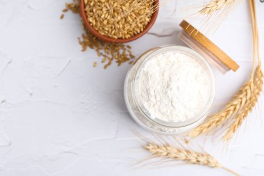 Cam kavanozda buğday unu, beyaz masada tahıl ve çiviler, düz konum. Metin için boşluk