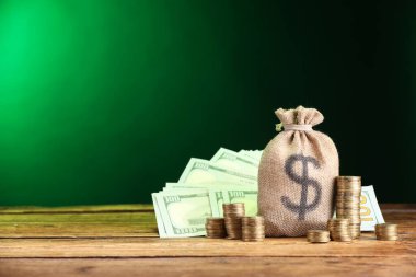 Çanta, dolar banknotları ve ahşap masaya istiflenmiş paralar yeşil eğimli arkaplan, metin için boşluk