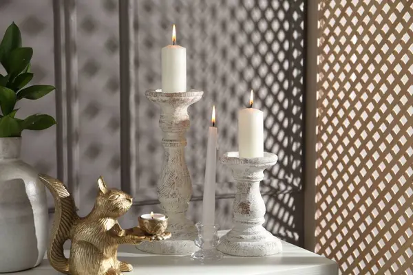 Zarif şamdanlar, yanan mumlar, vazoda dallar ve gri duvarın yanındaki şifoniyerde diğer dekorlar.
