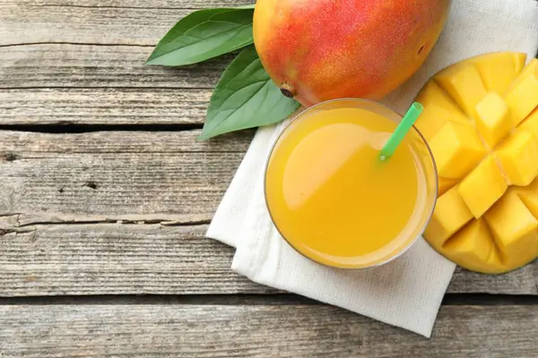 Lezzetli mango suyu bardakta, taze meyve ve yapraklar ahşap masada, düz yerde. Metin için boşluk