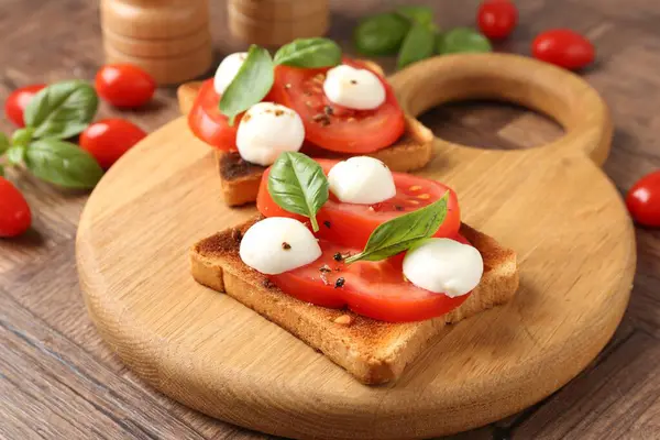 Mozarella peynirli, domatesli ve ahşap masadaki fesleğenli lezzetli sandviçler.