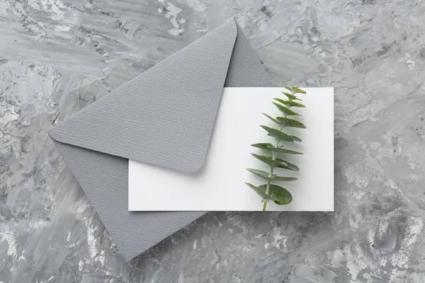 Boş davetiye kartı, gri desenli masa üzerindeki şube ve zarf, üst görünüm