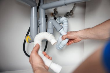 Tesisatçı, lavabonun altındaki boruları tamir ediyor. Kapalı.