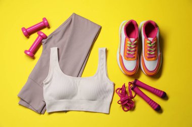 Spor kıyafetleri, halterler, spor ayakkabıları ve sarı arka planda ip atlama, düz uzanma