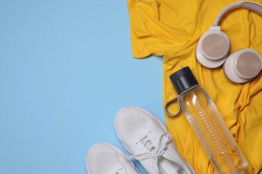 Spor kıyafetleri, bir şişe su, kulaklık ve açık mavi arka planda spor ayakkabıları, düz yatış.