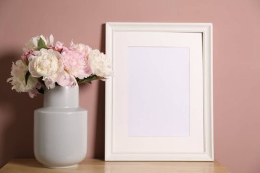 Vazodaki güzel şakayıklar ve pembe duvarın yanındaki ahşap şifoniyerin üzerindeki resim çerçevesi. Metin için boşluk