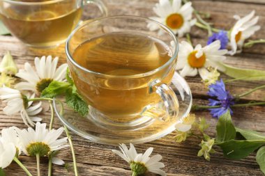 Cam bardaklarda aromatik bitki çayı, ahşap masada nane ve çiçekler, yakın plan.