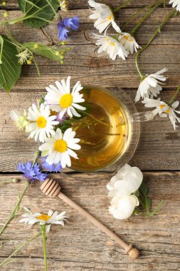 Cam bardakta Aromatik bitkisel çay, çiçekler ve ahşap masa, düz yatıyordu.