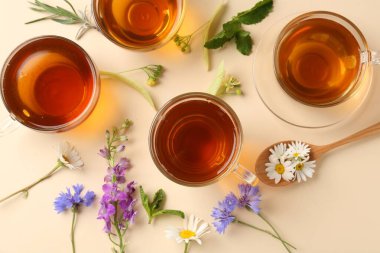 Cam fincanlarda aromatik bitki çayı ve bej arka planda farklı çiçekler.