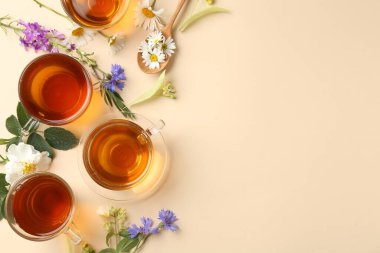 Cam fincanlarda aromatik bitki çayı ve bej arka planda farklı çiçekler, düz yatak. Metin için boşluk