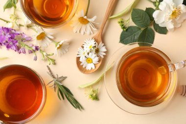 Cam fincanlarda aromatik bitki çayı ve bej arka planda farklı çiçekler.