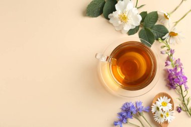 Cam fincanda aromatik bitki çayı ve bej arka planda farklı çiçekler. Metin için boşluk