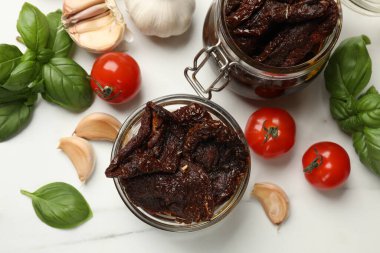 Lezzetli güneşte kurutulmuş domatesler, taze sebzeler, fesleğen ve sarımsak beyaz masada, düz yatıyordu.