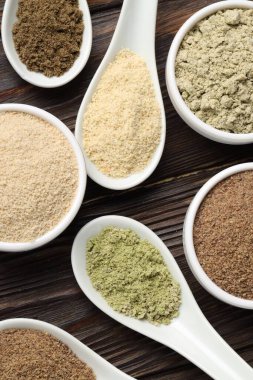 Farklı süper yiyecek tozları kaşık ve kaseler halinde ahşap masa, düz uzanmış
